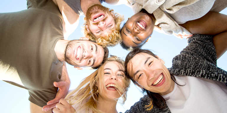 Fünf Jugendliche stehen im Kreis und schauen fröhlich lachend von oben herab in die Kamera.